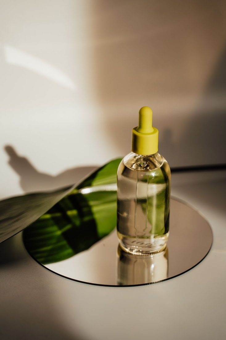 A glass dropper bottle on a reflective round surface.