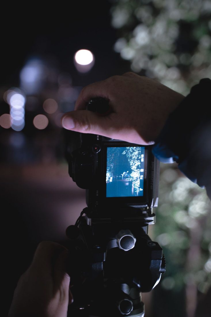 Hands operating a camera outdoors at night.