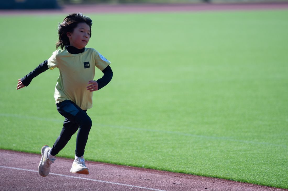 A child running on a track beside a green field.