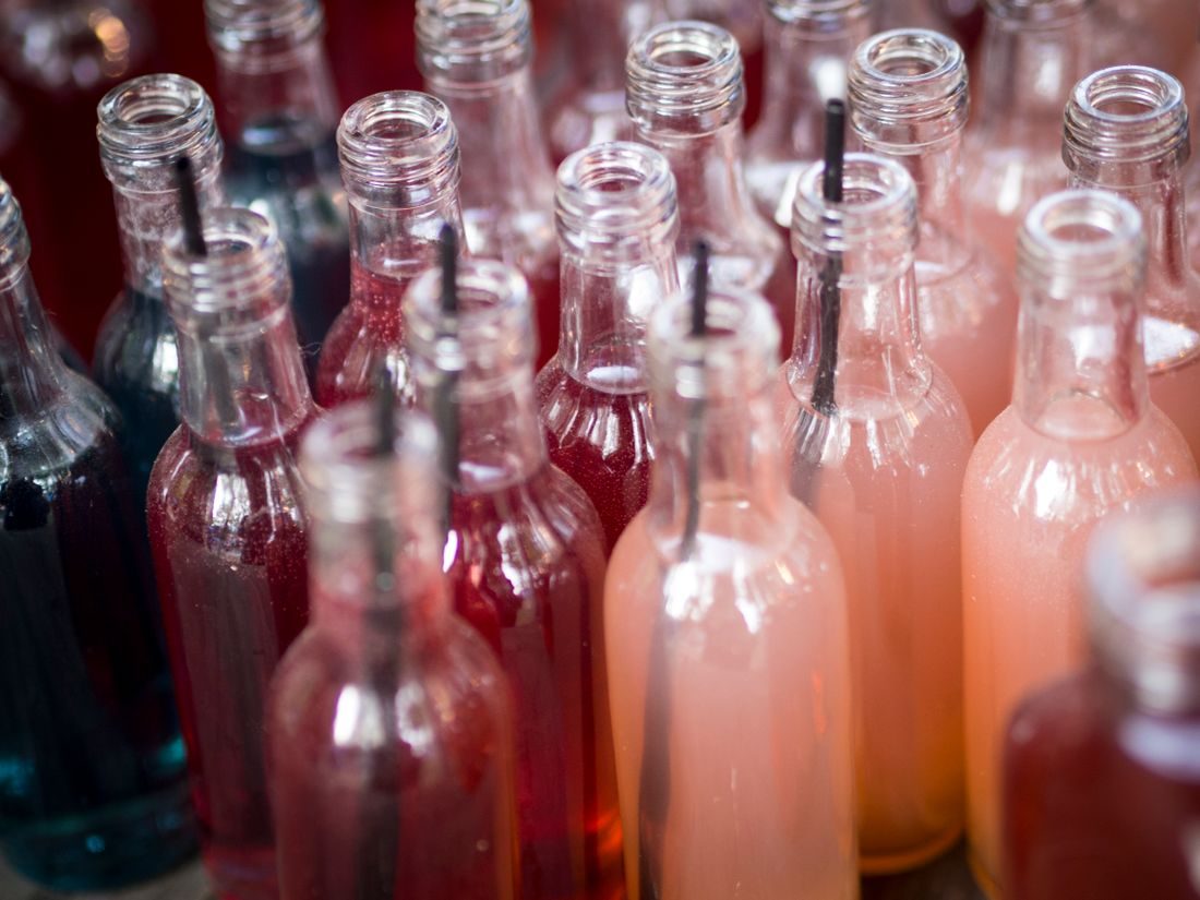 Clear glass bottles filled with drinks in several colours.