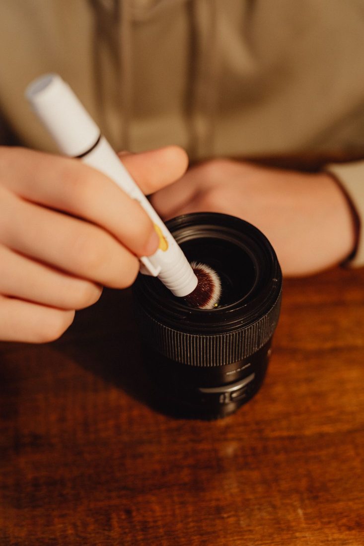 A hand using a cleaning tool on a camera lens.