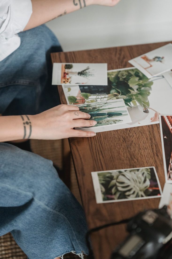 Hands comparing printed photographs on a wooden table.