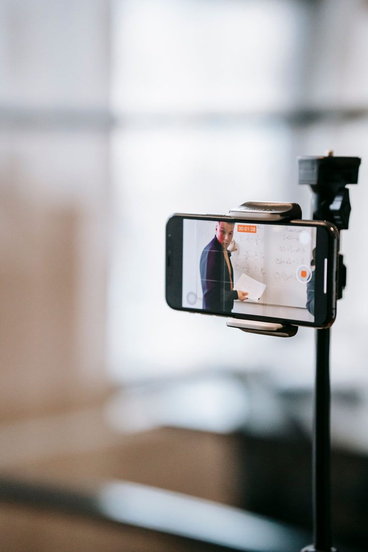 A mounted phone recording a presenter beside a whiteboard.