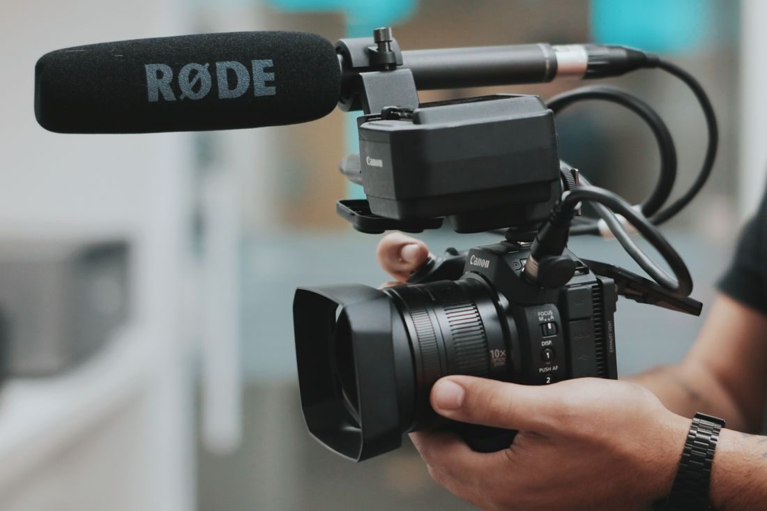 Hands supporting a video camera fitted with a microphone.