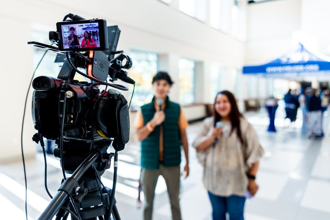 A video camera aimed at two people holding microphones.
