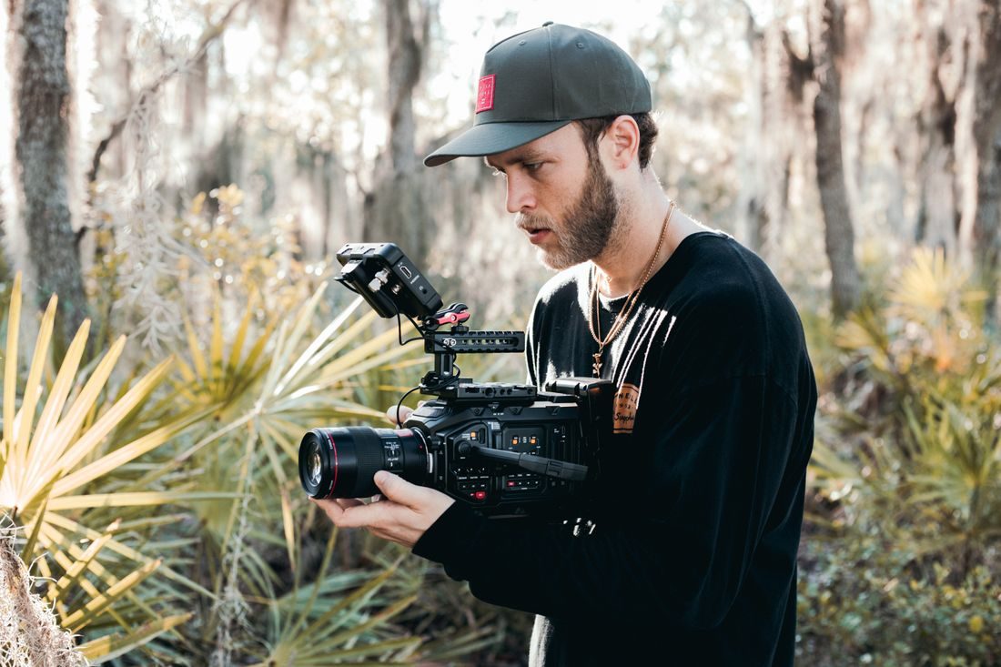 A camera operator working among trees outdoors.