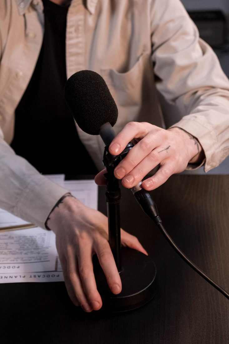 Hands adjusting a black microphone on a desk stand.