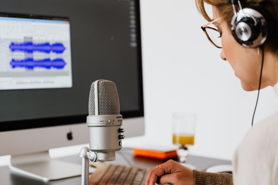 A woman wearing headphones beside a microphone and audio screen.