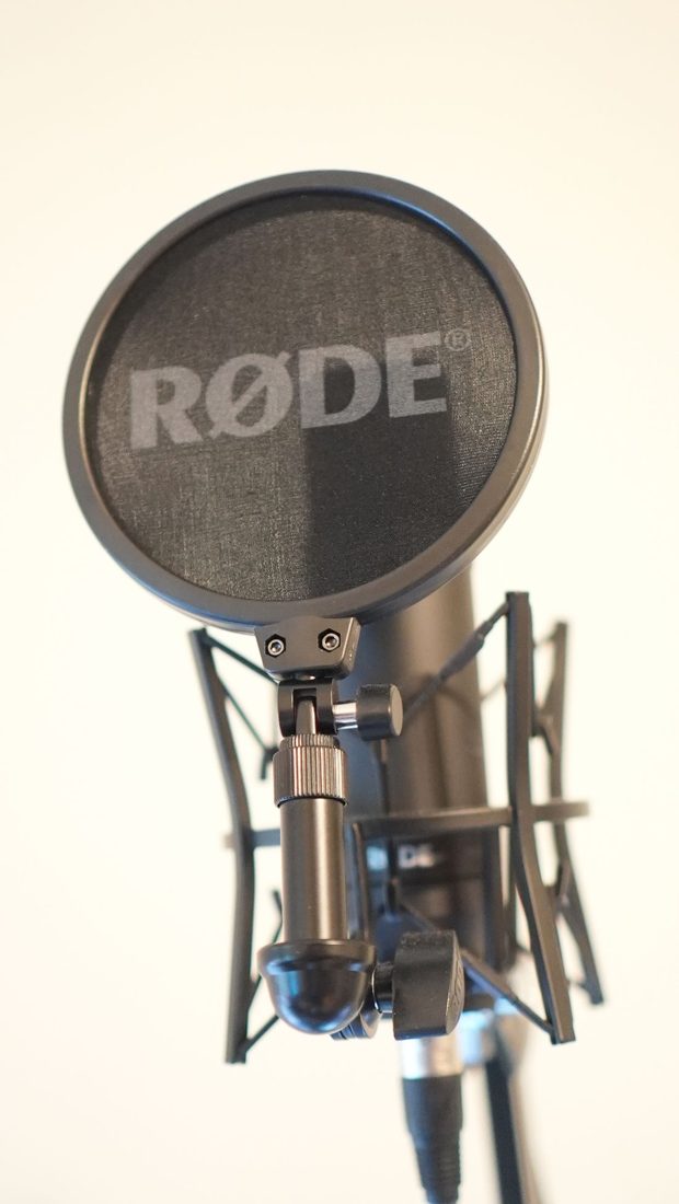 A microphone positioned behind a round pop filter.