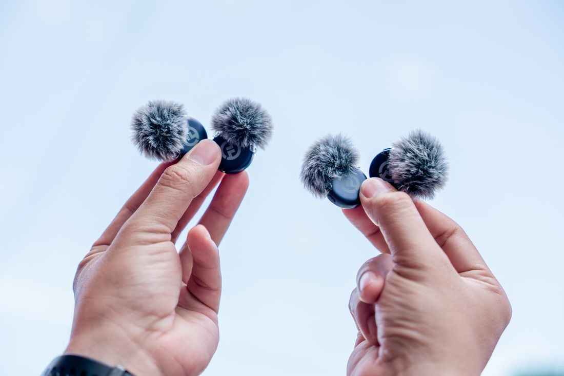 Hands holding small furry microphone wind protectors.