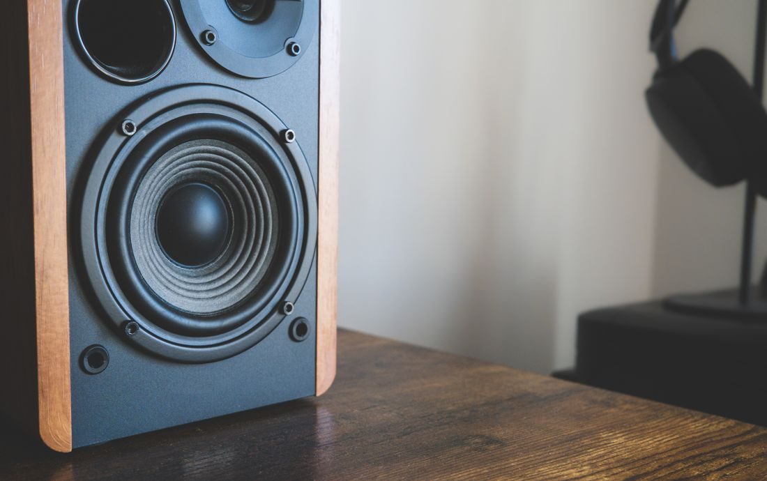 A studio speaker on a wooden desk with headphones nearby.