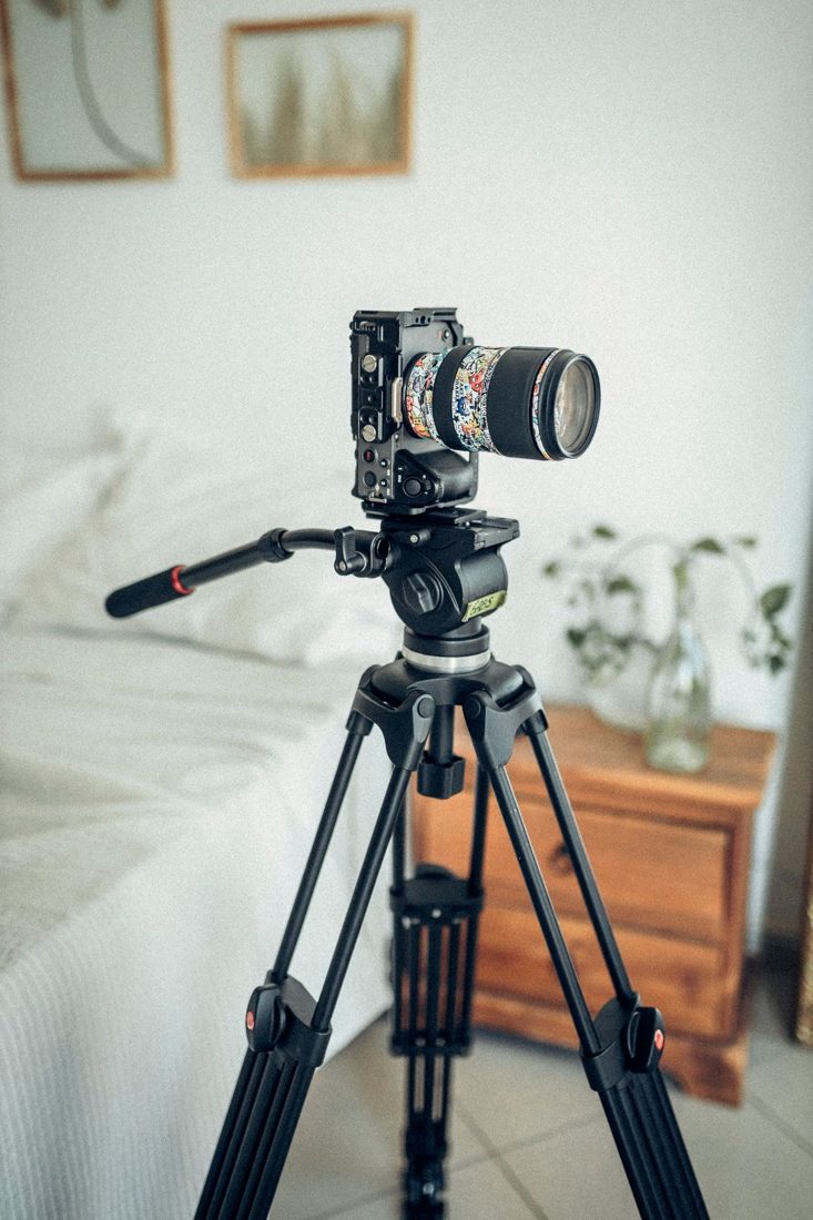 A camera on a tripod beside a bed.