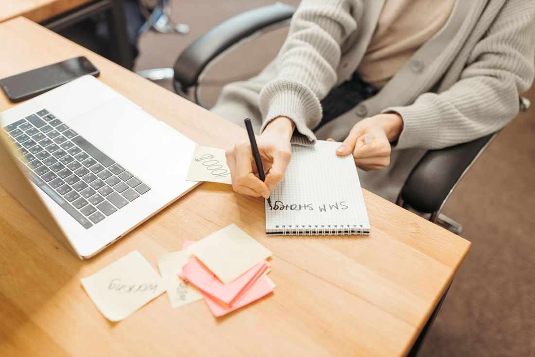 A person writing notes beside a laptop and sticky notes.