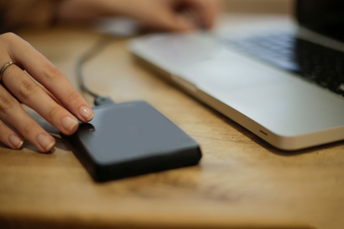 A hand connecting an external drive beside a laptop.