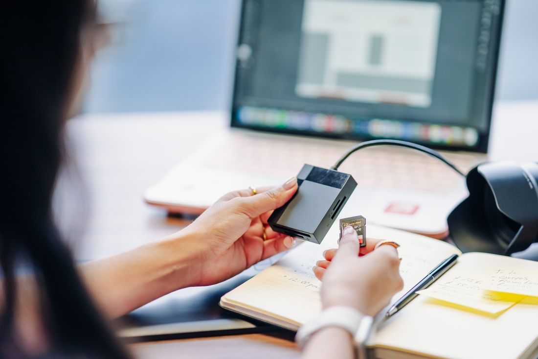 A person using a memory card reader beside a laptop.