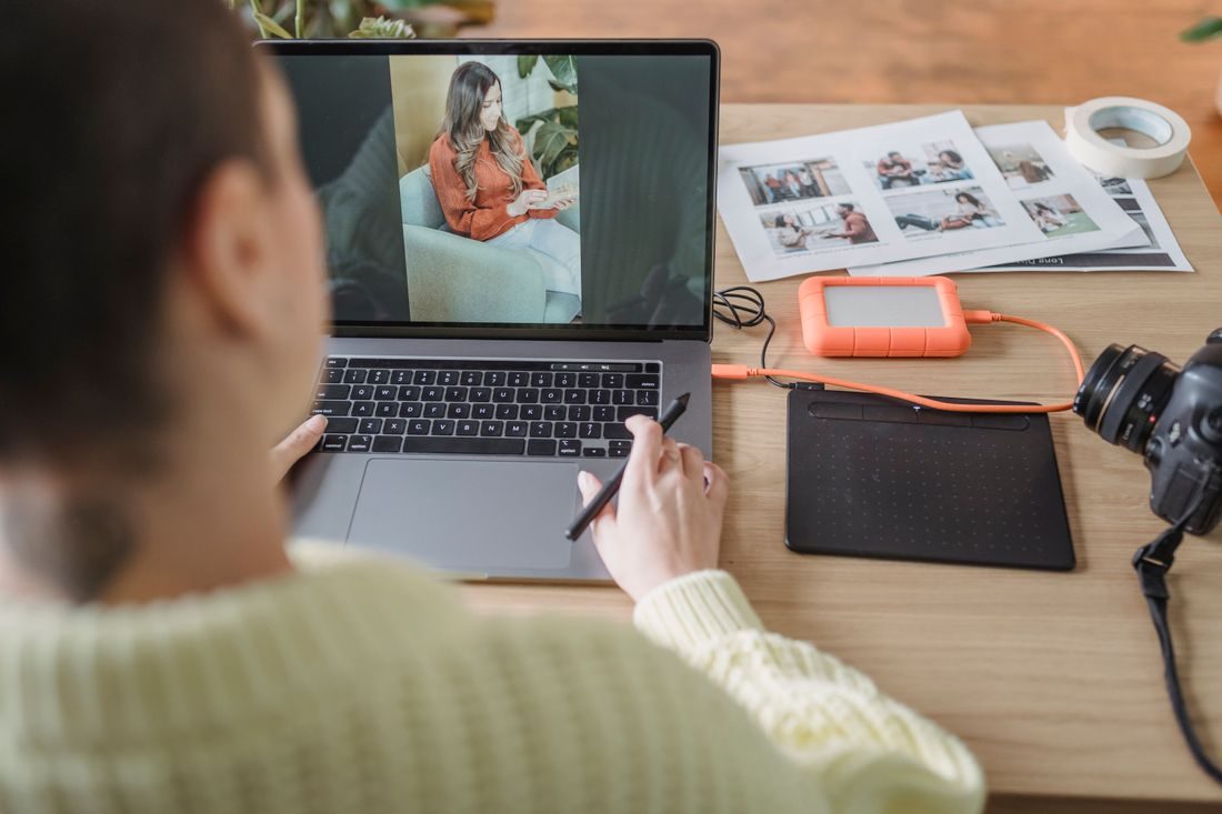 A person editing a photograph on a laptop beside printed images.