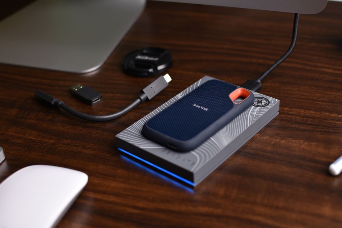 A portable external SSD and USB cables on a wooden desk.