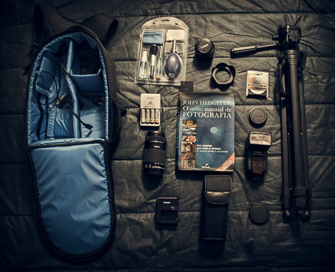 A camera bag, camera and accessories arranged on a wooden floor.